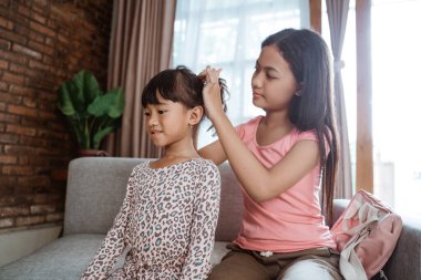 Kardeşinin saçını taramasına yardım eder.