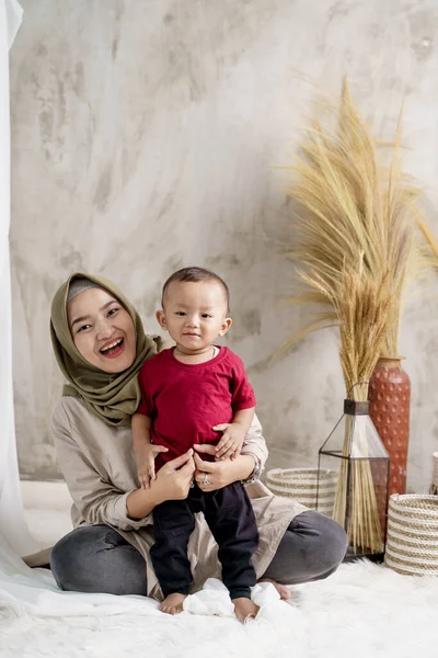 Asiatische junge Mutter und Sohn lächeln, als sie sich hinsetzen — Stockfoto