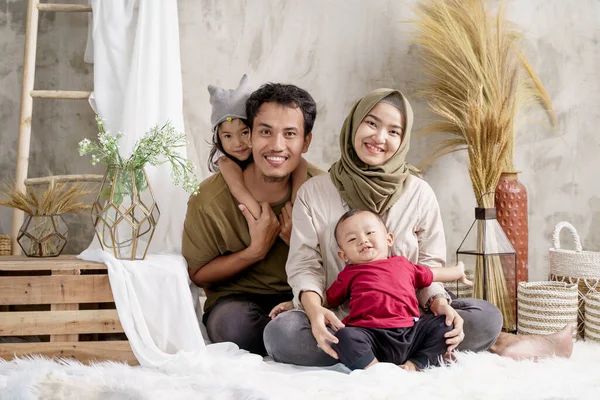 Padre, madre y dos niños cómodamente se sientan en la alfombra con sonrisa —  Fotos de Stock