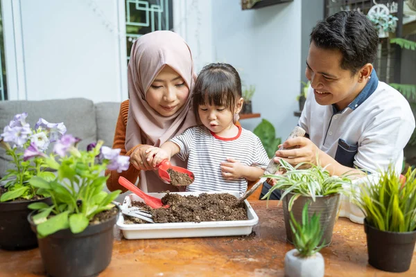 Putri dibantu oleh ibunya dengan memegang sekop kecil untuk mengambil tanah dan ayahnya memegang sekop kecil — Stok Foto