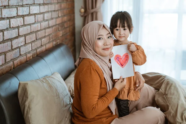 Gesluierde moeder en klein meisje glimlach terwijl het vasthouden van papier met een afbeelding van het hart als een symbool van liefde — Stockfoto