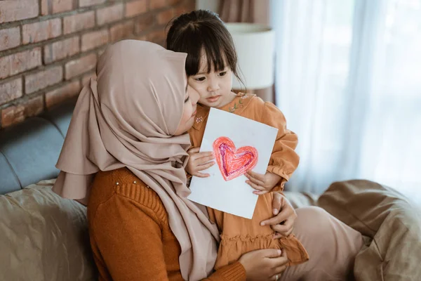 Ibu terselubung mencium gadis kecil sambil memeluk dan memegang hati dicetak kertas — Stok Foto