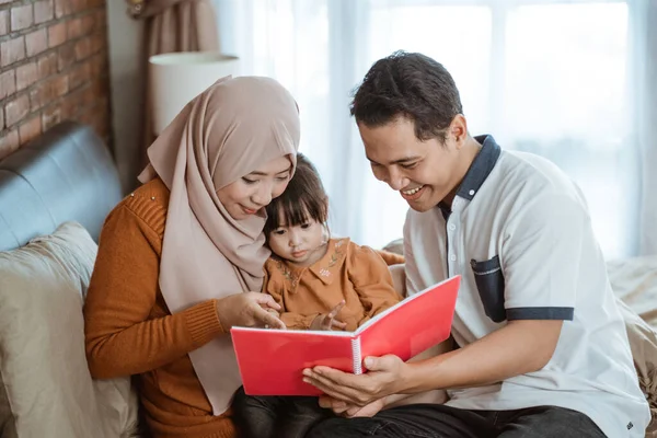 Mamãe e papai sorriem segurando um livro quando vêem um livro de histórias com a filha — Fotografia de Stock