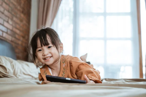 Asyalı küçük kız kameraya bakıp telefonu tutarken mutlu bir şekilde gülüyor. — Stok fotoğraf