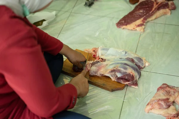 Mãos de mulheres adultas que cortam carne de sacrifício em uma tábua de corte de madeira — Fotografia de Stock