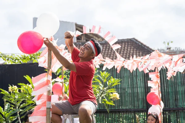 Anak muda dalam kemeja merah dan merah dan putih ikat kepala duduk di tangga untuk mendirikan balon — Stok Foto