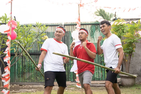 Tiga pemuda Asia dengan atribut merah dan putih dan memegang bambu berduri — Stok Foto