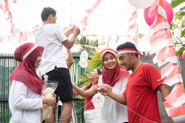 Pemuda Asia dan wanita muda mengikat tali untuk menggantung kerupuk dalam persiapan untuk Crecker Eating kontes — Stok Foto