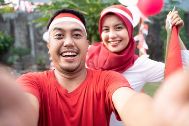 Genç çift fotoğraf makineleriyle selfie çekerken kırmızı ve beyaz özellikler takıyor.
