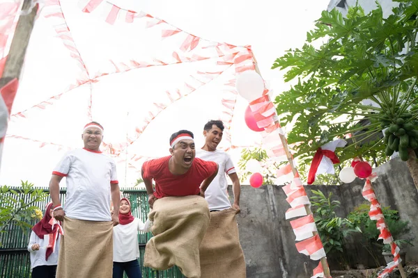 Üç genç adam mutlu bir şekilde çuval yarışına katıldı ve bitiş çizgisine doğru hızla sıçradı.
