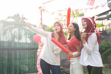 Konfeti ve küçük bayraklı üç Asyalı kız akıllı telefon kamerasıyla selfie çekerken bir araya geldiler.