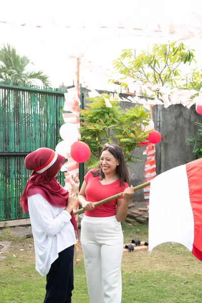 Dua gadis dengan jilbab dan ikat kepala merah dan putih memegang tongkat bambu dengan bendera Indonesia — Stok Foto