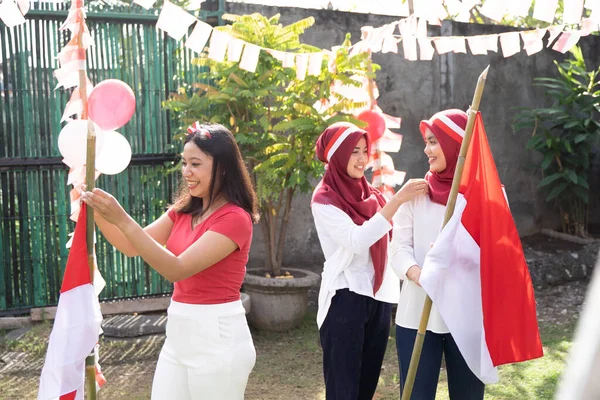 Tiga perempuan Asia tersenyum sambil memasang bendera dan ikat kepala Indonesia — Stok Foto