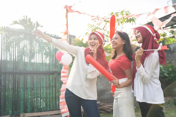 Három vidám lány piros-fehér ruhát visel, akik mobiltelefonnal csinálnak szelfit. — Stock Fotó