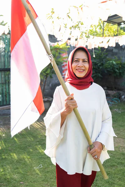 Hijab avó segurando uma vara de bambu com bandeira indonésia — Fotografia de Stock