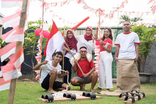 Kelompok teman-teman berkumpul mengenakan pakaian merah dan putih membawa bendera Indonesia dengan tongkat bambu dan peralatan perlombaan — Stok Foto