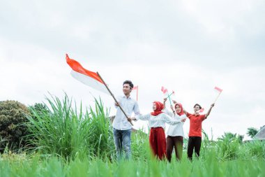 Beyaz giyen Asyalı genç adam Endonezya bayrağı taşıyor ve arkadaşları onun arkasından yürüyor.