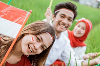 Asyalı kız gülümseyerek elinde küçük kırmızı beyaz bir bayrak olan kamerayı görüyor pirinç tarlasının ortasında oturuyor.
