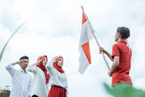 Asiatisk ung man i rött bär en indonesisk flaggad pinne och tre av hans vänner i en salut — Stockfoto