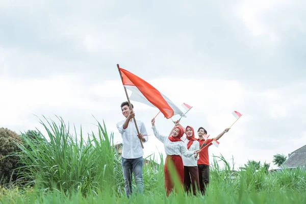 Chłopiec w bieli chodzi niosąc indonezyjską flagę z kijem i jego przyjaciele idą za nim — Zdjęcie stockowe