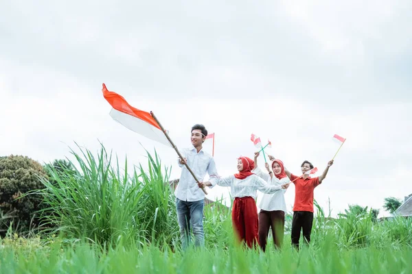 Asiatisk ung man i vitt promenader bär en indonesisk flagga och hans vänner går bakom honom — Stockfoto