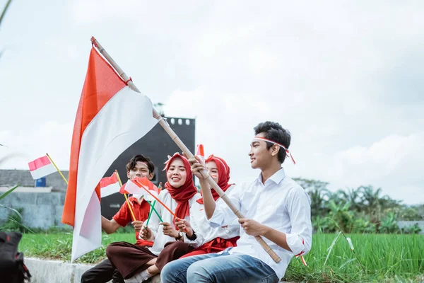 Pemuda duduk membawa tongkat dengan bendera Indonesia dan teman-temannya duduk di sampingnya — Stok Foto