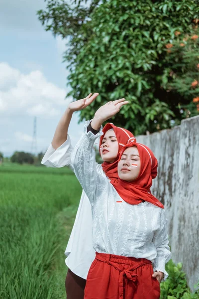 Dwie zasłonięte dziewczyny noszące czerwone i białe atrybuty podniósł jedną rękę, aby uniknąć promieni słonecznych — Zdjęcie stockowe