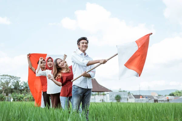 Jonge mannen en vrouwen die de Indonesische vlag voeren terwijl zij rood en wit dragen de attributen die op een rij in de rijstvelden staan — Stockfoto