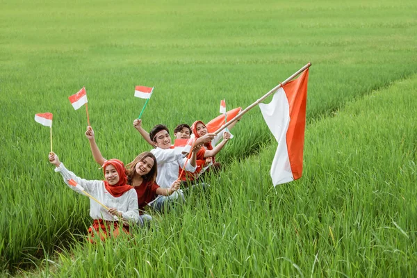 Divertindo-se juntos de jovens marchar no campo de arroz segurar bandeira indonésia — Fotografia de Stock