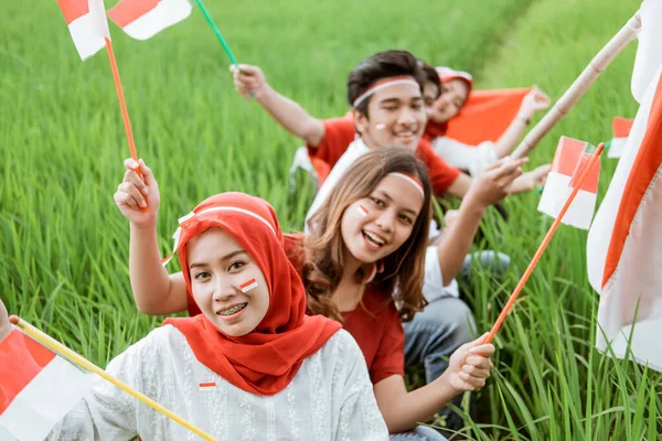 Nahaufnahme von jungen Männern und Frauen, die die indonesische Flagge halten und schwenken, während sie auf den Reisfeldern rot-weiße Attribute tragen — Stockfoto