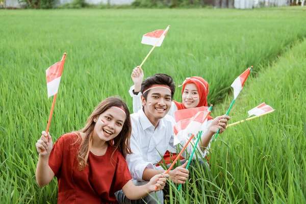 Tre asiatiska vänliga leende poserar hålla en liten flagga sitter i mitten av risfält — Stockfoto