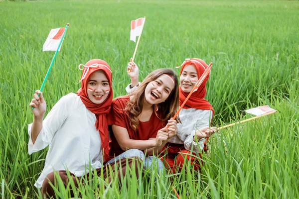 Tiga gadis tersenyum dan berdiri memegang bendera indonesia dengan atribut — Stok Foto