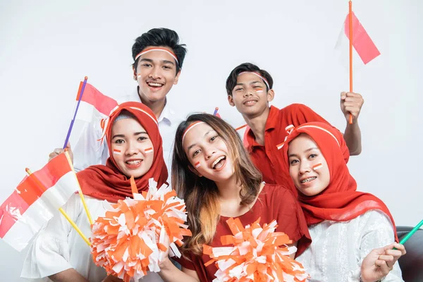 Grupo de jóvenes asiáticos sonriendo sosteniendo pompón y banderas pequeñas sentados en el sofá — Foto de Stock