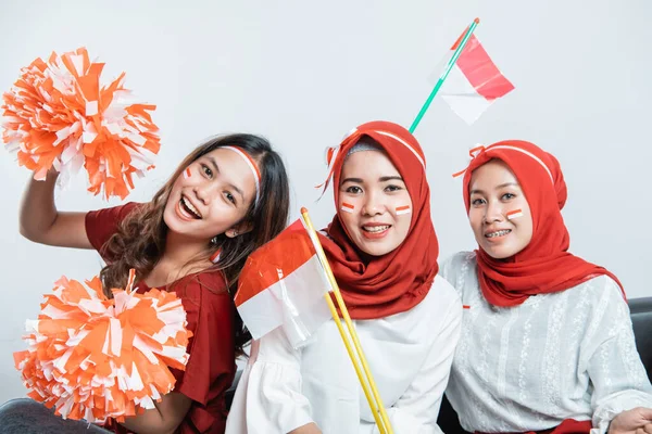 Tres amistosas mujeres jóvenes sonriendo sosteniendo pompón y banderas pequeñas —  Fotos de Stock