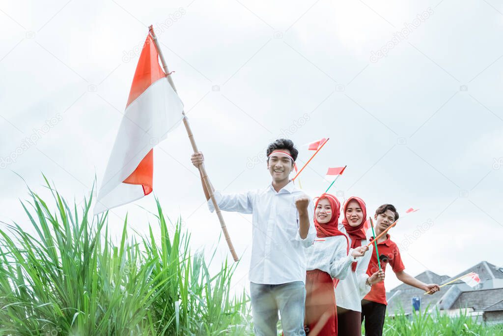 asian young man in white carrying raise an Indonesian flag and his friends behind follow him