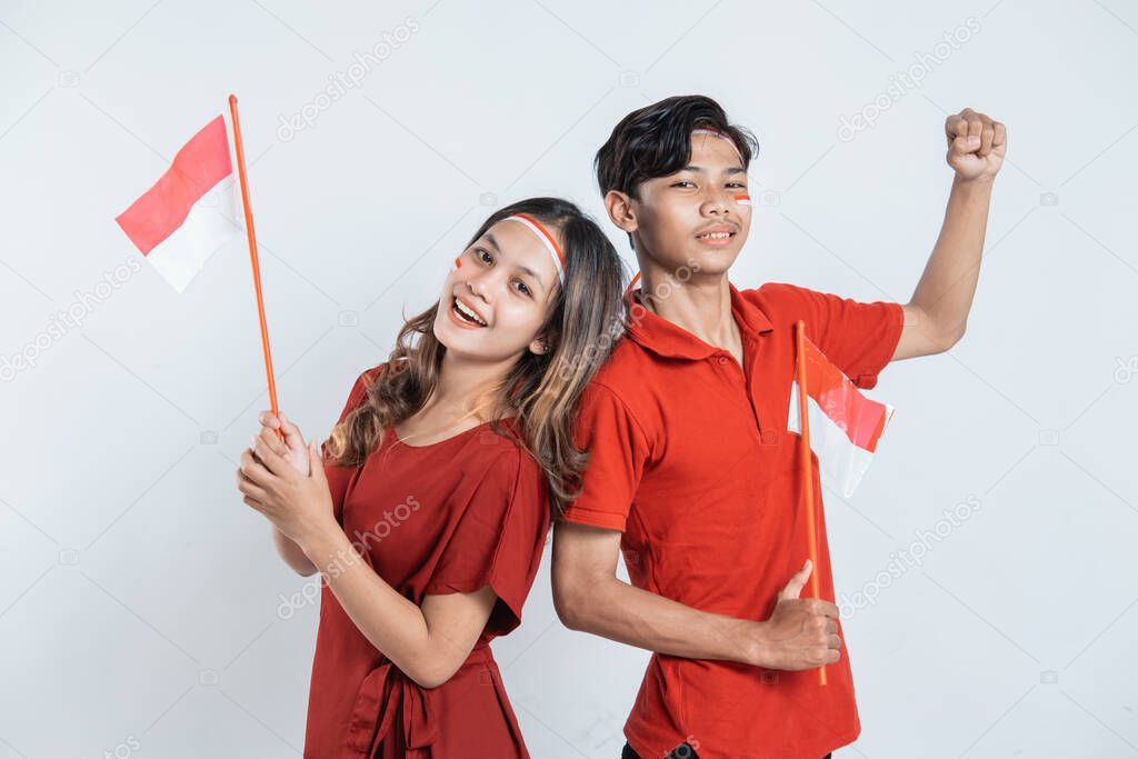girl and boy stand wearing red and white attributes and hold small Indonesian flags