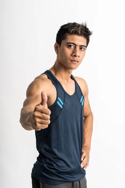 Muscular jovem vestindo estande de camisa de ginástica de frente para o lado com os polegares até a câmera — Fotografia de Stock