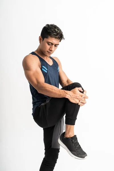 Hombre muscular que lleva puestos de ropa deportiva frente a un lado hacer estiramiento de la pierna levantando la pierna delante del estómago — Foto de Stock
