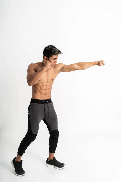 Celkový obraz mladého muže s svalnatým tělem s útočícím pohybem jednou rukou úder — Stock fotografie