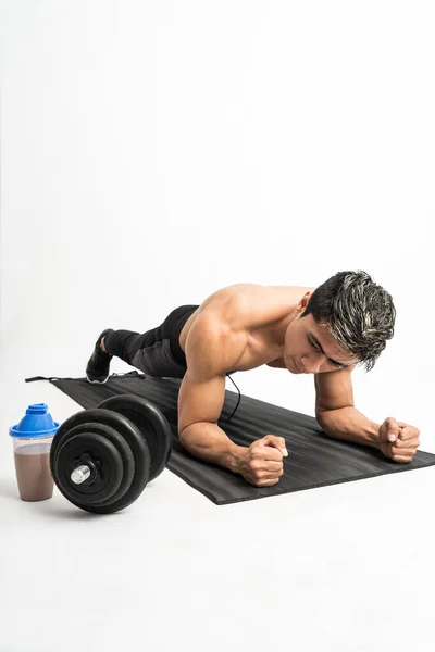 Homem muscular sem roupas fazer exercícios de prancha com um tapete ao lado da garrafa e haltere — Fotografia de Stock