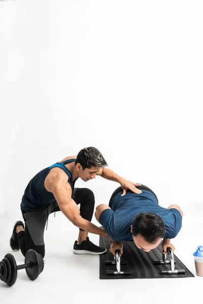 Treinador acompanha um homem fazendo exercícios push-up segurando para fazer os movimentos certos — Fotografia de Stock