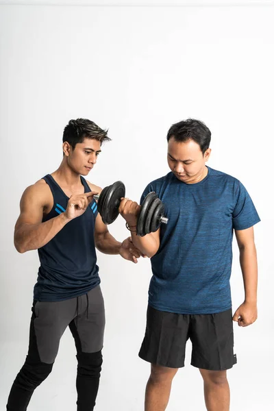 Entraîneur accompagne un homme haltère de levage pour les exercices de biceps avec tenir la main pour faire les bons mouvements — Photo