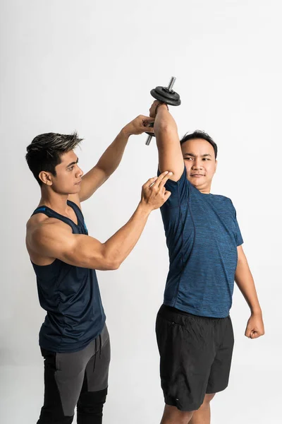 Trainer begeleidt een man tillen halter voor triceps oefeningen met de hand om de juiste bewegingen te maken — Stockfoto