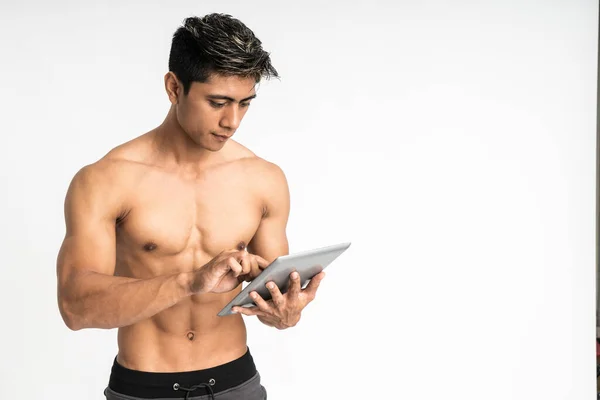 Asiatico giovane con muscolare corpo in possesso di un tablet con due mano digitando stand rivolto in avanti e guardare un tablet con copyspace — Foto Stock