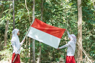 Kırmızı ve beyaz bayrak taşıyan iki küçük Müslüman kız ve bayrak sallayan başka bir kız.