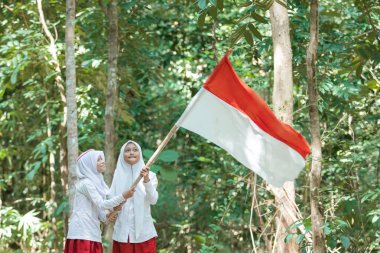 Peçeli iki küçük Müslüman kız ellerinde büyük kırmızı beyaz bir bayrak tutuyorlar ve bayrak sallıyorlar.