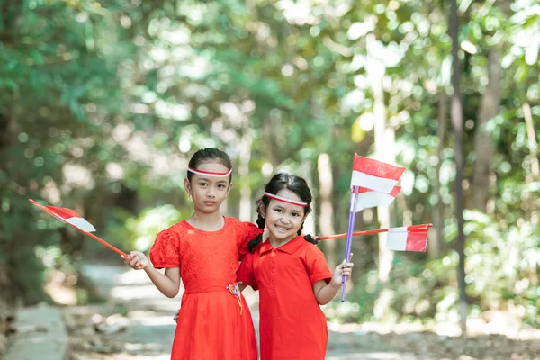 Två små flickor stående i röd skjorta och rött och vitt attribut med röda och vita flaggor — Stockfoto