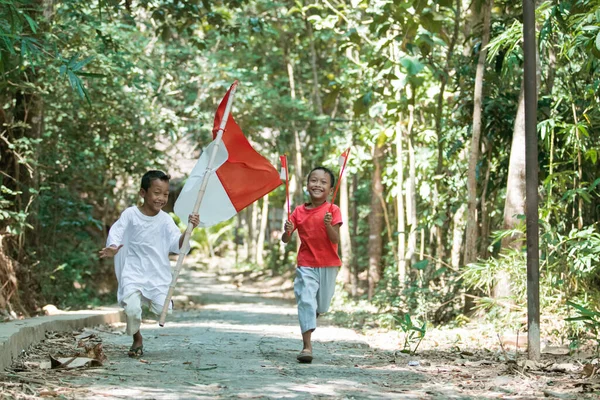 Dua anak laki-laki asia berlari ketika memegang bendera merah dan putih dan mengibarkan bendera — Stok Foto