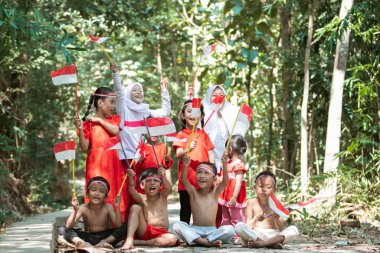 Asyalı çocukların kırmızı ve beyaz bayrak tutup birlikte kaldırdığı eğlenceli bir grup.