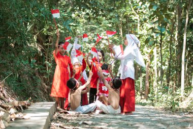 Bir grup çocuk ellerinde küçük kırmızı ve beyaz bayrak tutuyorlar ve birlikte yükseltiyorlar.